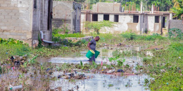 EkoLakay client carrying waste containers through flood waters