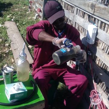 SOIL intern, Wenley Moïse, extracting samples from the liquid filters installed underneath SOIL's composting bins to take to the lab for testing.
