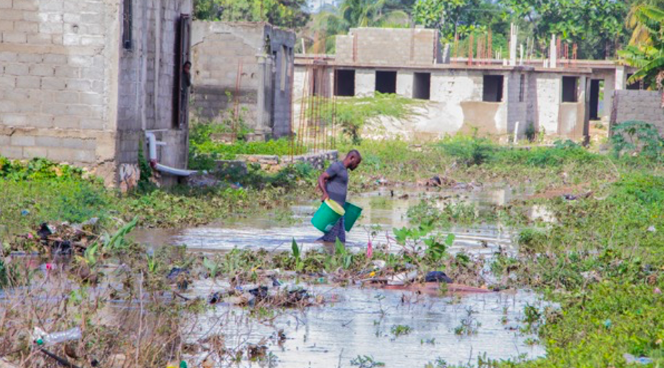 EkoLakay client carrying waste containers through flood waters